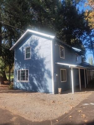 Blue two-story house with white trim and porch in a wooded yard