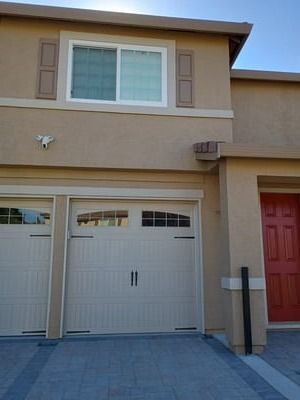 Exterior of a beige townhouse with a white garage door, upper window, and red front door