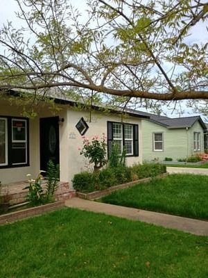 Single-story beige house with green shutters, front porch, and a green lawn.