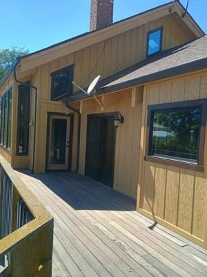 Wooden house exterior with deck, large windows, and sloped roof under clear blue sky