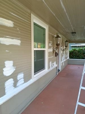 Covered walkway with beige siding, white-trimmed windows, and a red concrete floor.