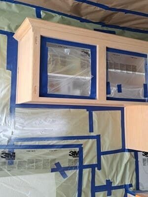 Painted cabinet with two blue-taped windows, covered in plastic for renovation.