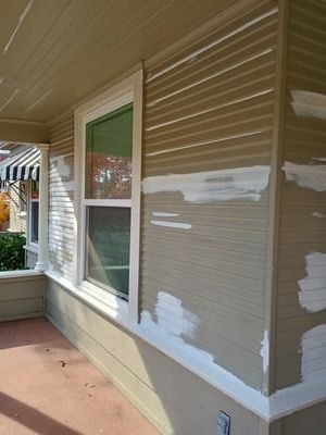 Beige house siding with fresh white patch repairs beside a window on a front porch
