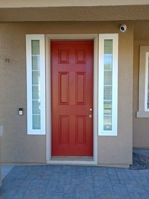 Red front door with narrow side windows on a beige house entryway.