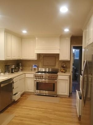 Bright kitchen with white cabinets, wood floor, stainless stove, and a doorway to another room.