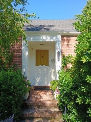 Brick house front entry with white doorframe, wooden door, and steps surrounded by greenery