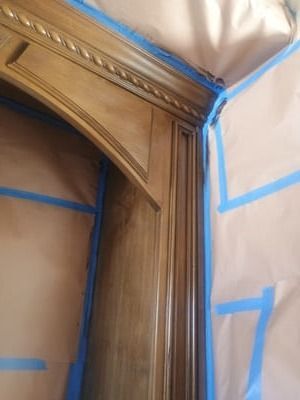 Close-up of a carved wooden door frame with blue painter’s tape and covered walls during renovation