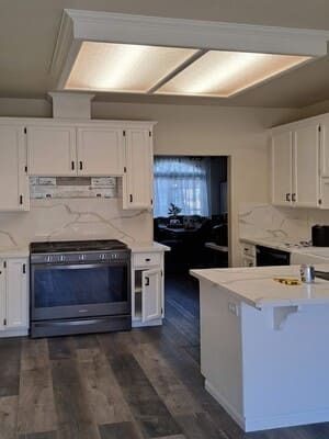 Bright modern kitchen with white cabinets, gray floor, island, and large ceiling light panel.
