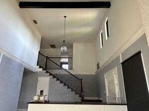 Tall foyer with staircase, white walls, dark railings, high ceiling, and hanging light fixture