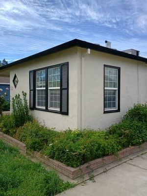 Small cream-colored house with black-trimmed windows and green shrubs along the base.