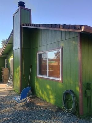 Green house exterior with a chimney, window, and coiled garden hose by the wall.