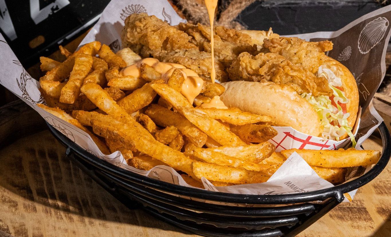 A sandwich and french fries in a basket on a table.
