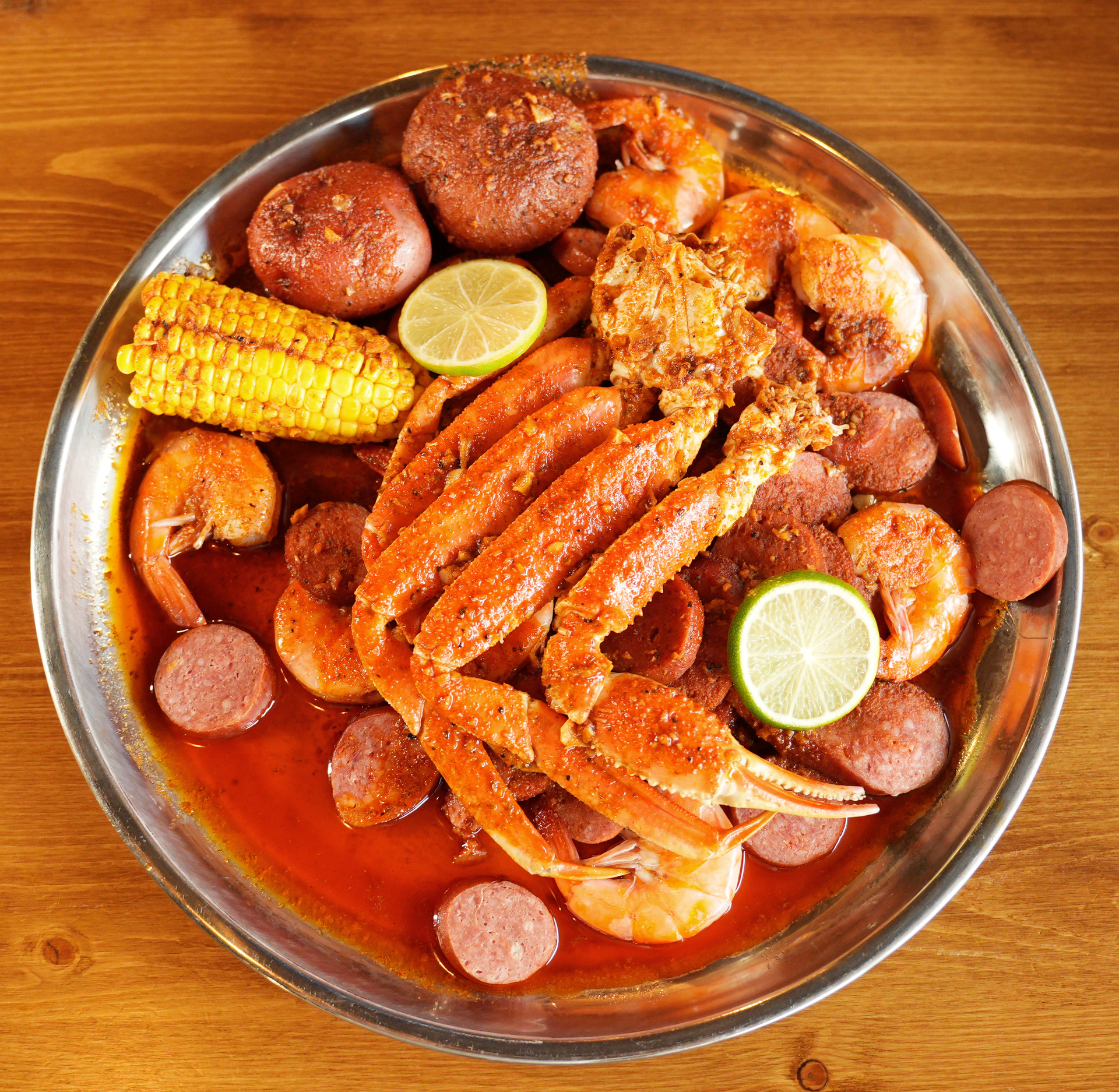 A plate of crab legs , shrimp , sausage , corn on the cob and potatoes on a wooden table.