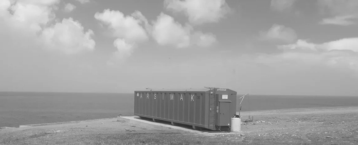 A blue dumpster is sitting on the shore of a beach next to the ocean.