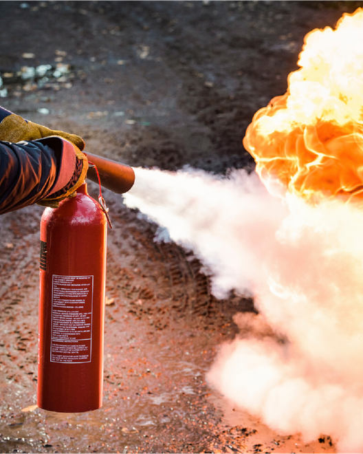 Una persona utilizza un estintore rosso per spegnere un grande incendio all'aperto.