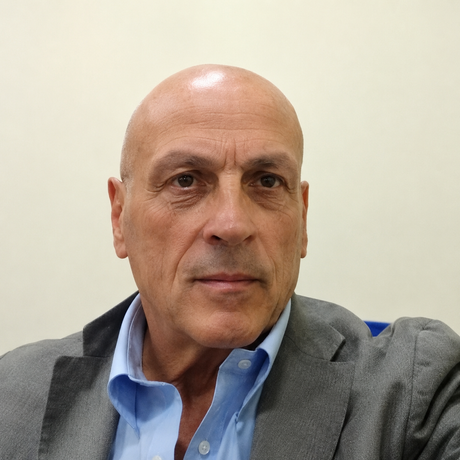 Uomo con camicia bianca abbottonata in piedi davanti a uno sfondo bianco uniforme.