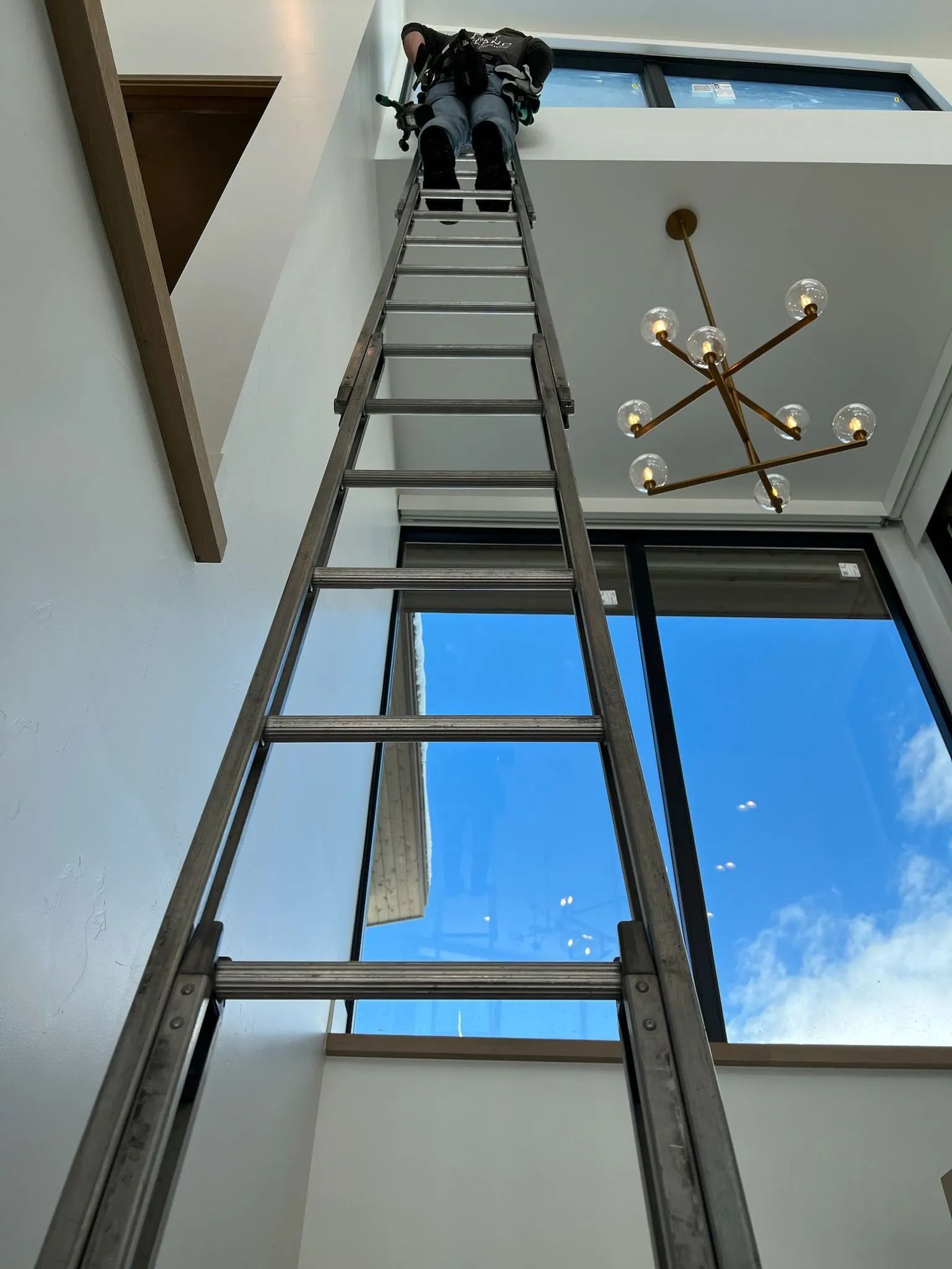 A man is standing on a ladder in a room with a chandelier.