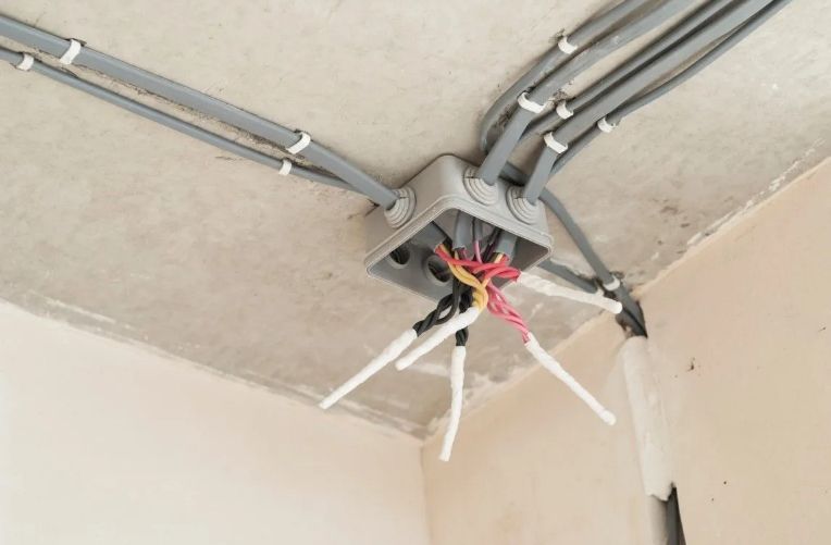 An open electrical junction box mounted on a ceiling, with multiple gray cables extending from it and exposed wires.