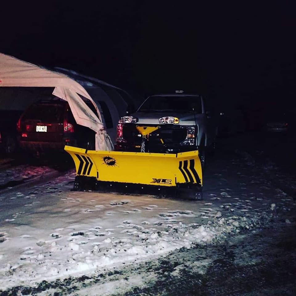 Un chasse-neige monté sur un camion dégage la neige de nuit. Le chasse-neige est jaune avec des détails noirs.