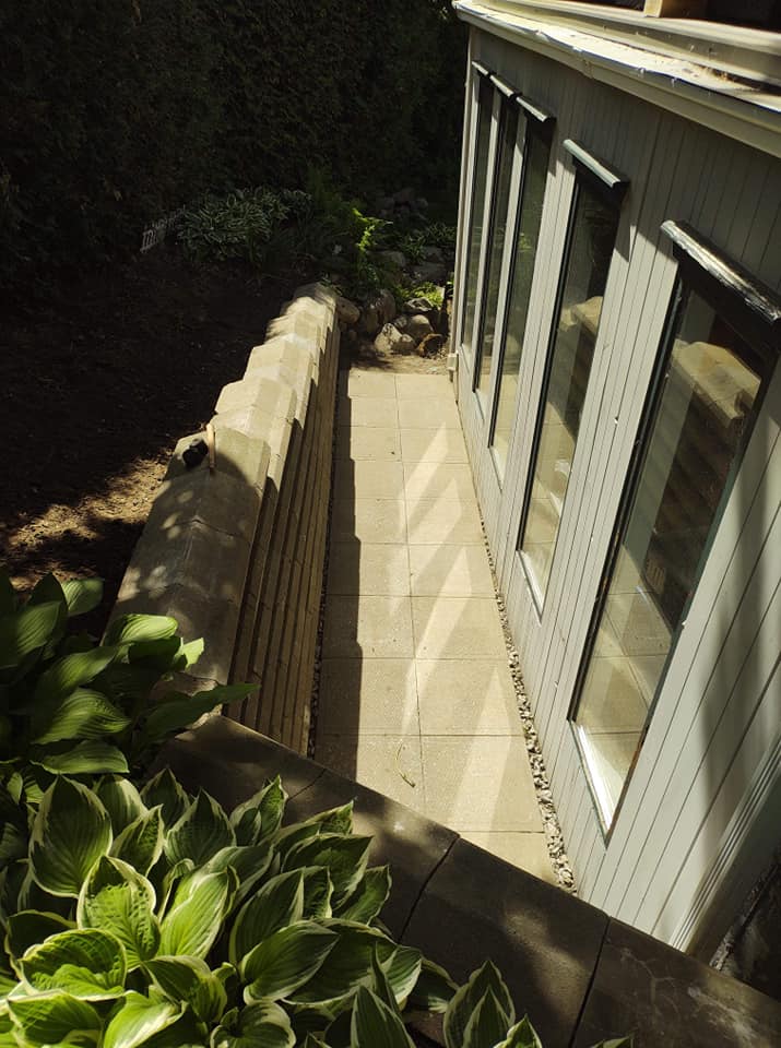 All&eacute;e pav&eacute;e avec bordure en bois longeant une maison avec portes vitr&eacute;es.