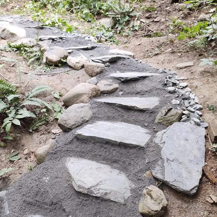 Des marches en pierre sont en construction dans un jardin, avec de grandes dalles plates et du gravier.