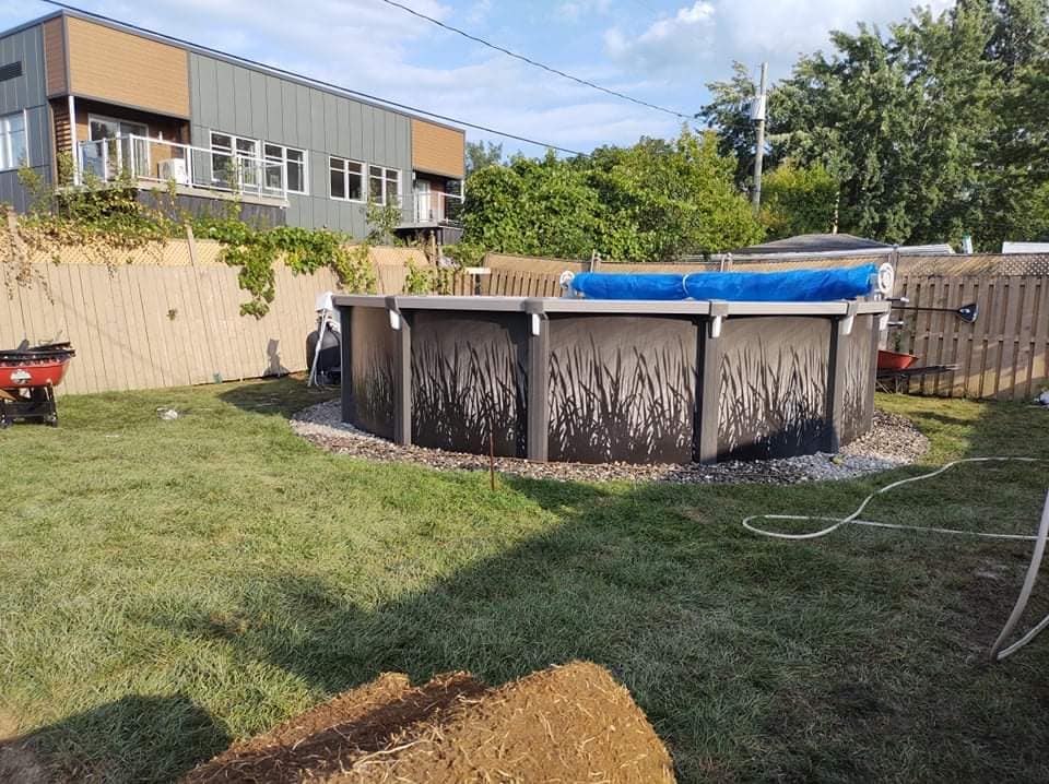 Piscine hors sol dans un jardin entouré d'une clôture et de pelouse. Couverture de piscine bleue visible.