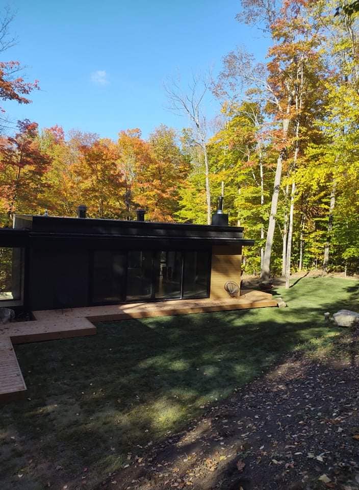 Chalet moderne aux parois de verre, entouré d'arbres aux couleurs automnales éclatantes sous un ciel bleu.