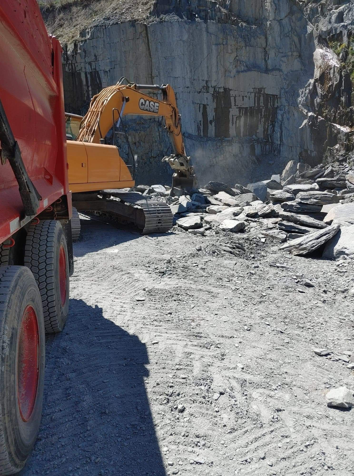Une excavatrice charge de l'ardoise dans un camion-benne rouge dans une carrière.