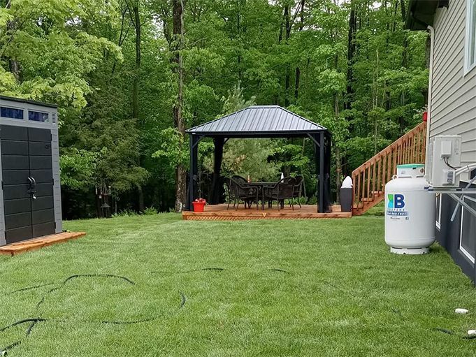 Pelouse avec kiosque, abri de jardin et citerne de propane. Arbres en arrière-plan.