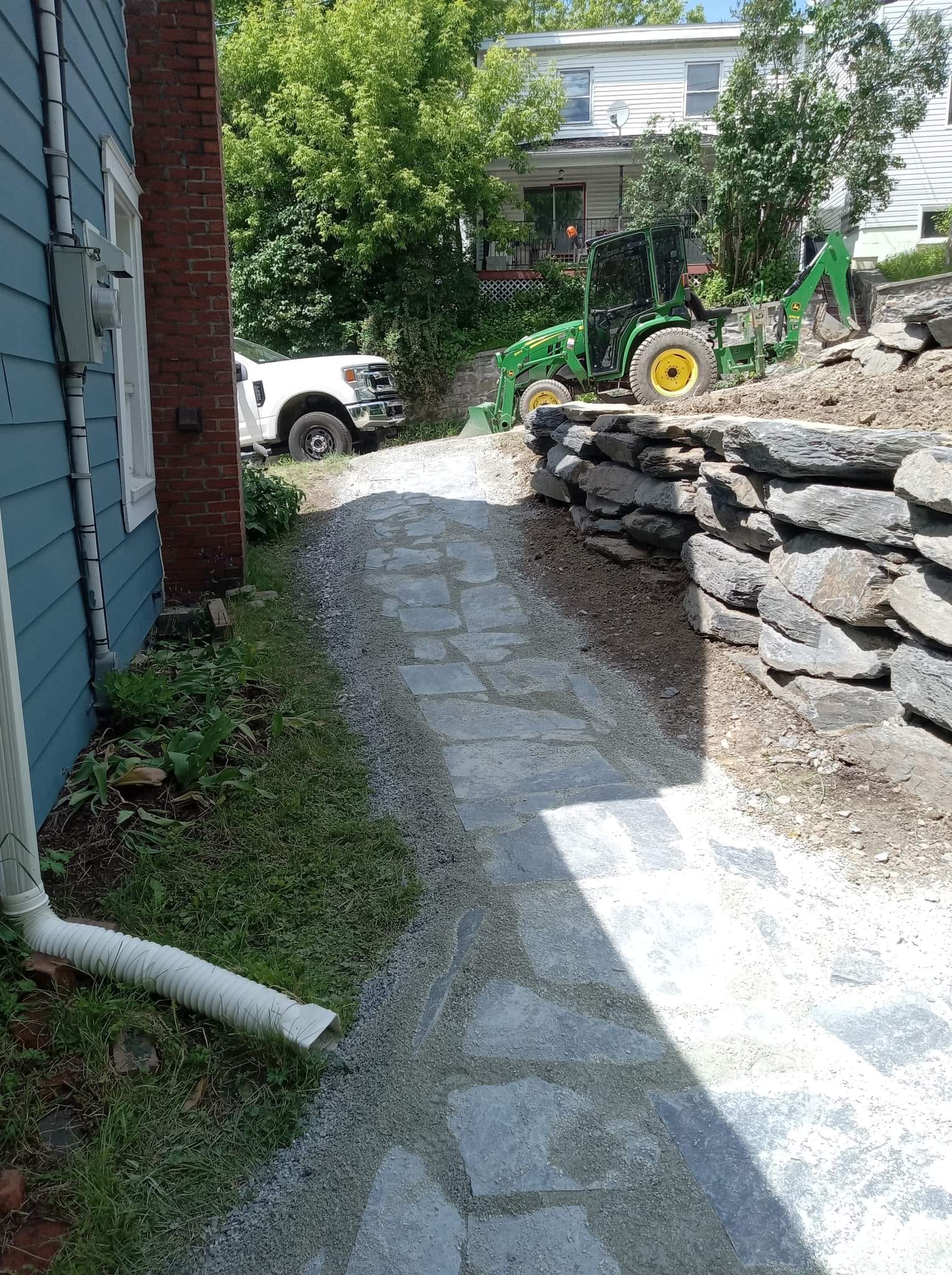 Allée en pierre grise avec pavés unis en cours de pose, équipement de chantier et camion en arrière-plan.