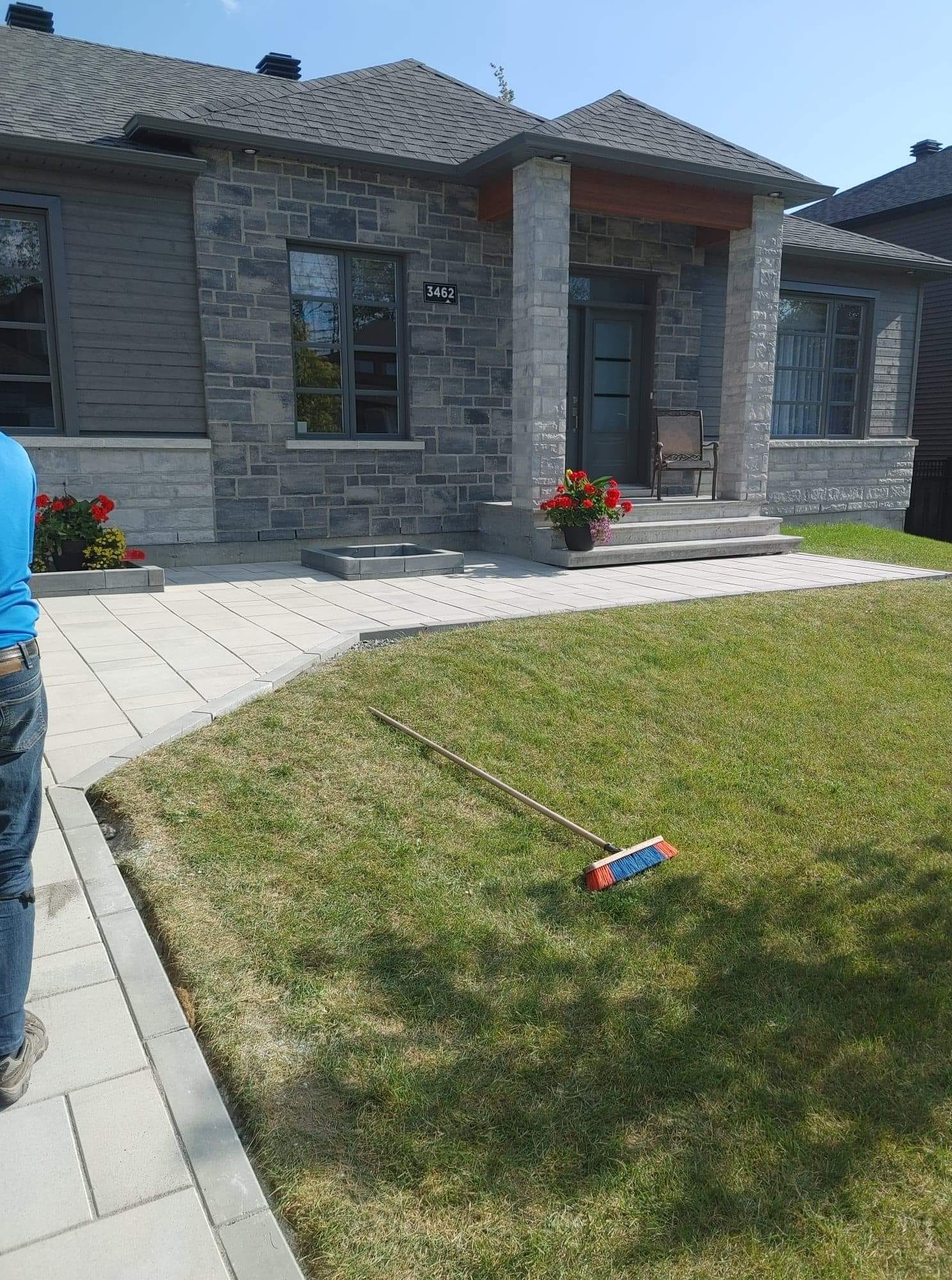Pelouse fra&icirc;chement pos&eacute;e devant une maison en pierre avec patio pav&eacute;.