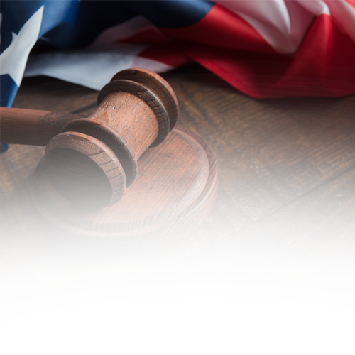 A wooden gavel sits on a wooden table in front of an american flag