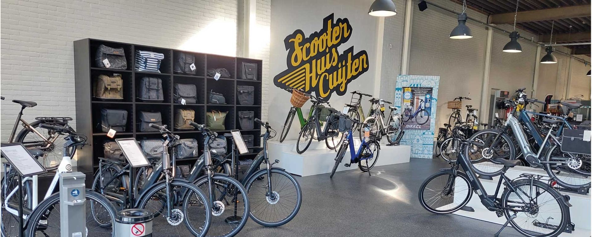 Twee mannen op e-bikes voor een fietsenwinkel met een logo.