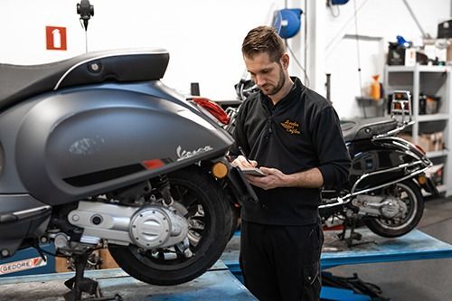 Twee mannen op e-bikes voor een fietsenwinkel met een logo.