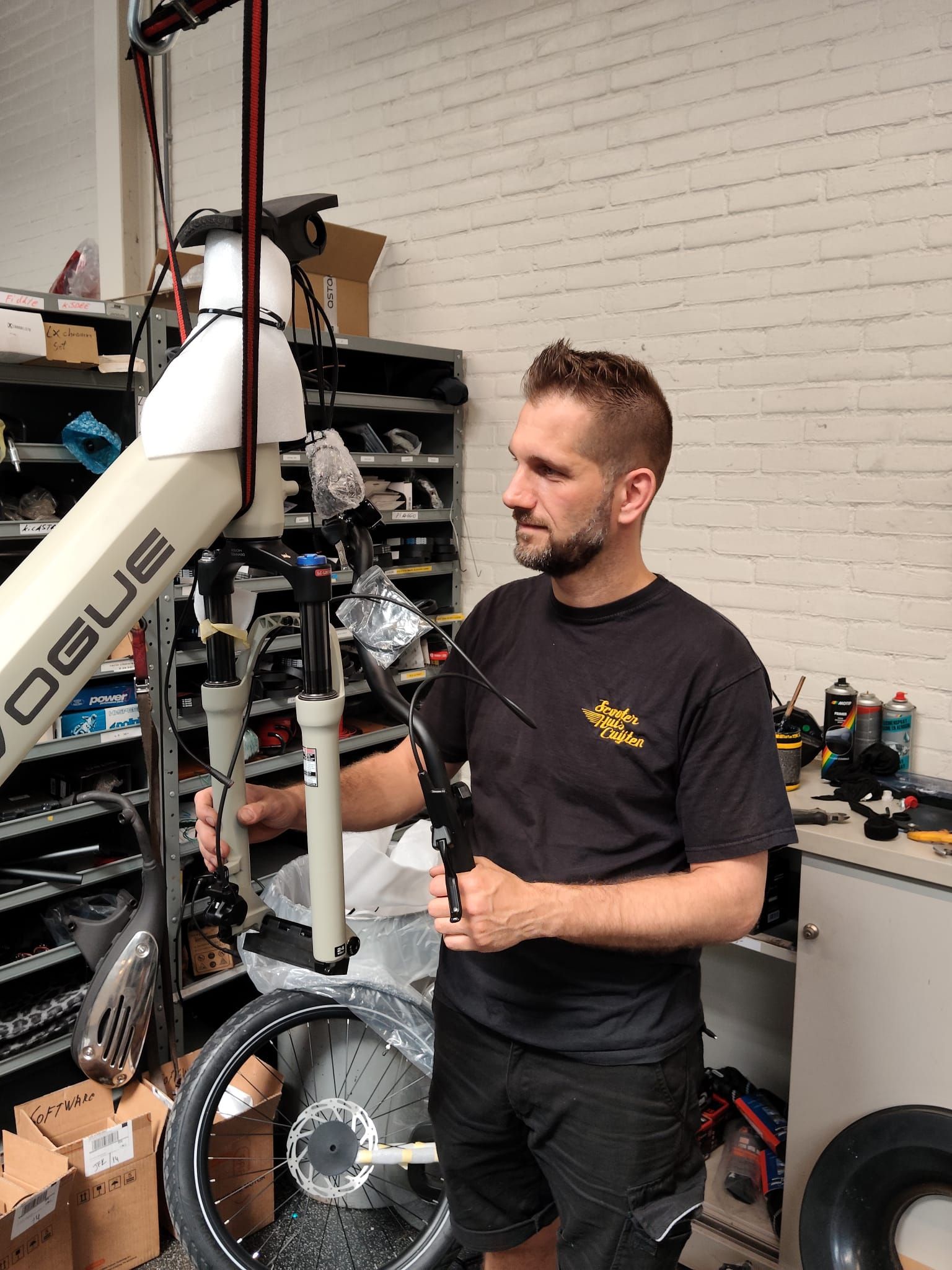 Twee mannen op e-bikes voor een fietsenwinkel met een logo.