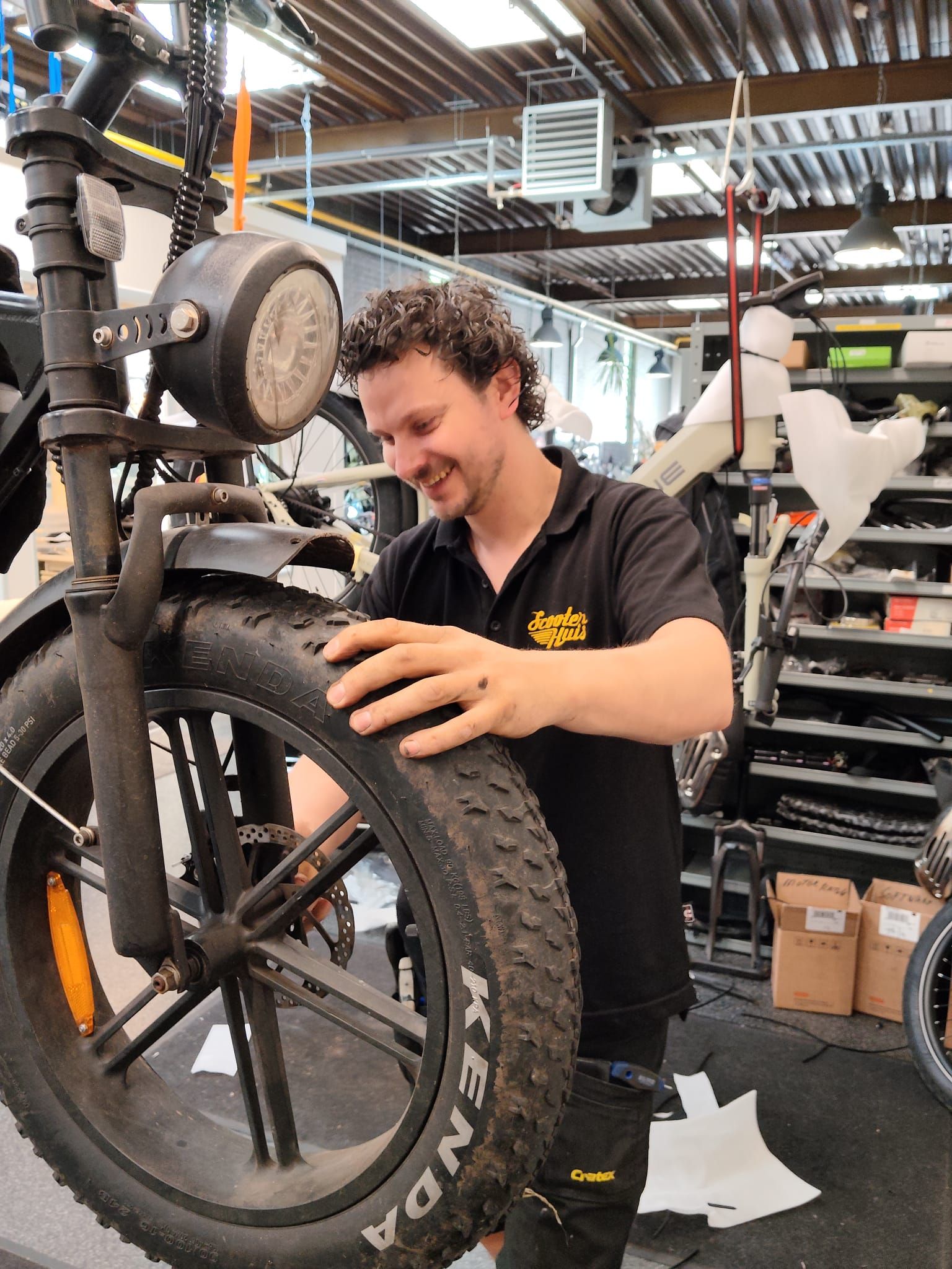 Twee mannen op e-bikes voor een fietsenwinkel met een logo.