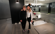 Two people standing in a yoga studio, smiling, with mats and mirrors in the background.