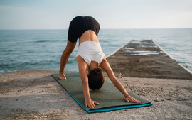 Person doing downward dog on a yoga mat on a pier by the ocean