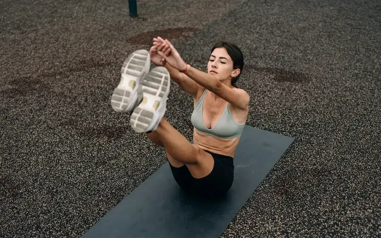 Woman in sportswear doing a V-sit on a yoga mat outdoors