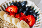 A bowl of oatmeal topped with banana slices, strawberries, blueberries, and oats.