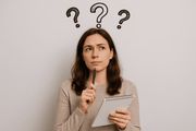 Person holding a pen and notepad, looking thoughtful with question marks above their head.