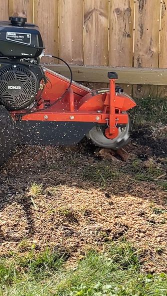 Red lawn mower cutting grass beside a wooden fence in a yard