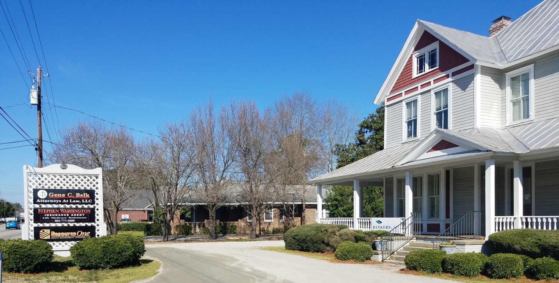 A two-story building with a porch, a sign, and trees under a clear blue sky.
