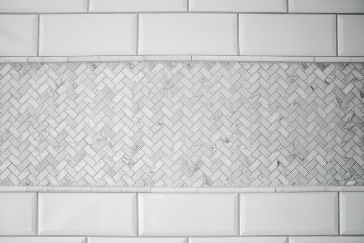 A close up of a white tile wall with a herringbone pattern.