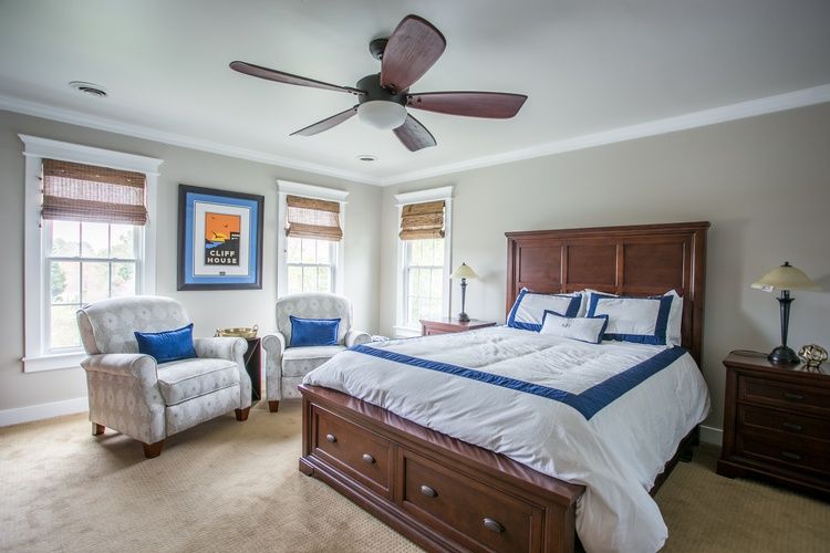A bedroom with a bed , chairs , nightstands and a ceiling fan.