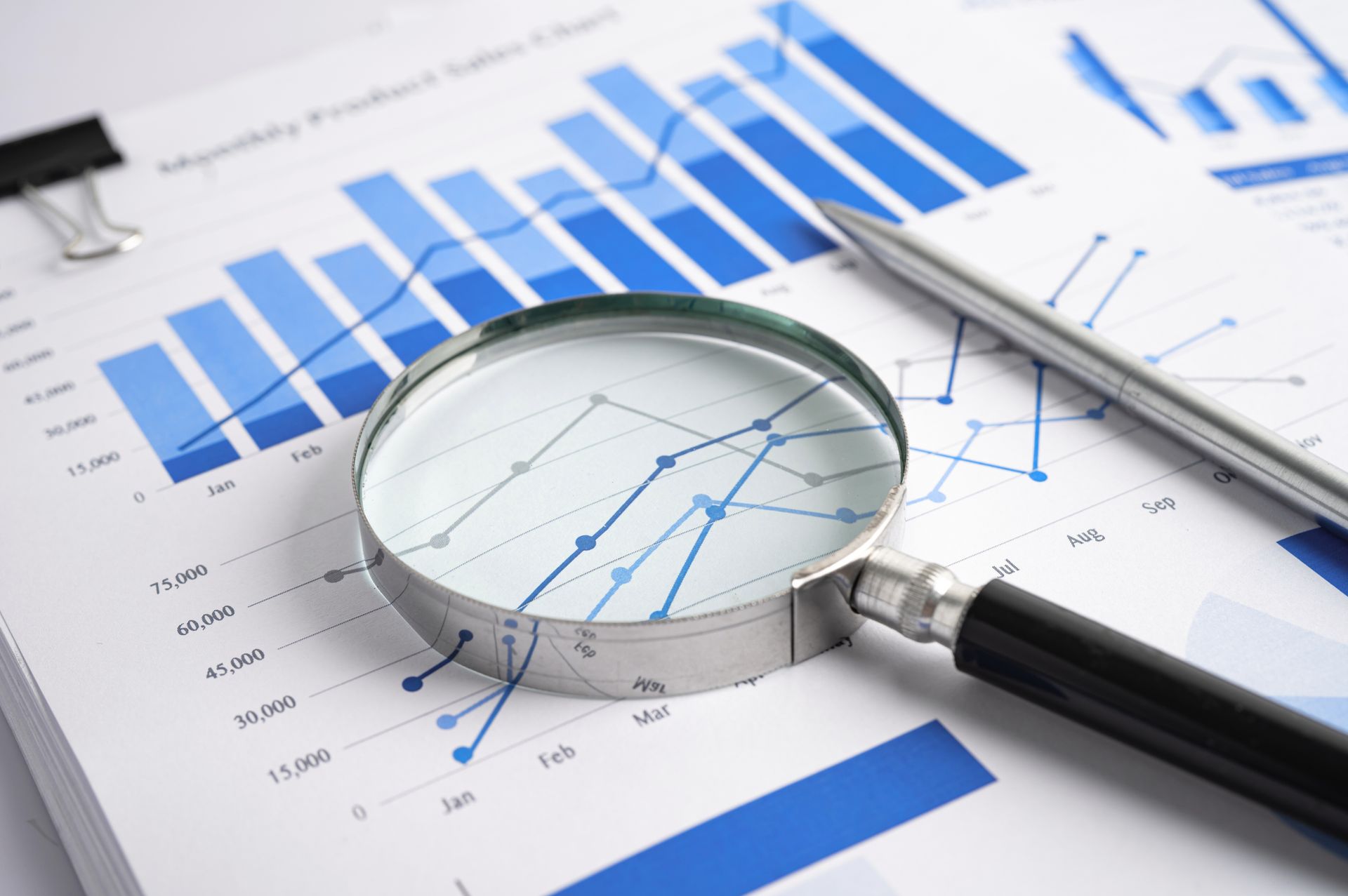 Magnifying glass on financial charts, analyzing sales data with a pen on the side. Magnifying glass on financial charts, analyzing sales data with a pen on the side.