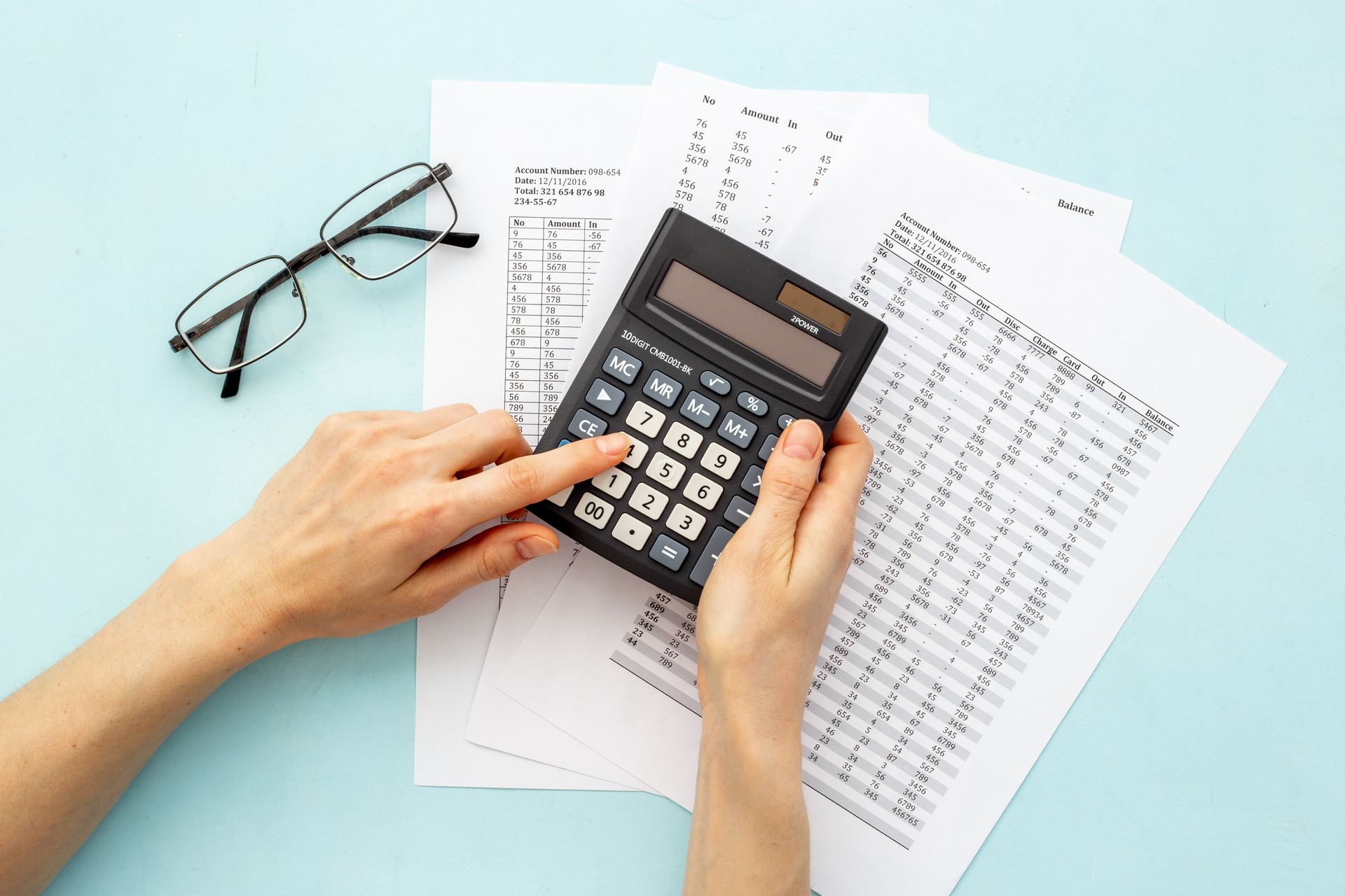 Hands using calculator, papers and eyeglasses on a blue background. Hands using calculator, papers and eyeglasses on a blue background.