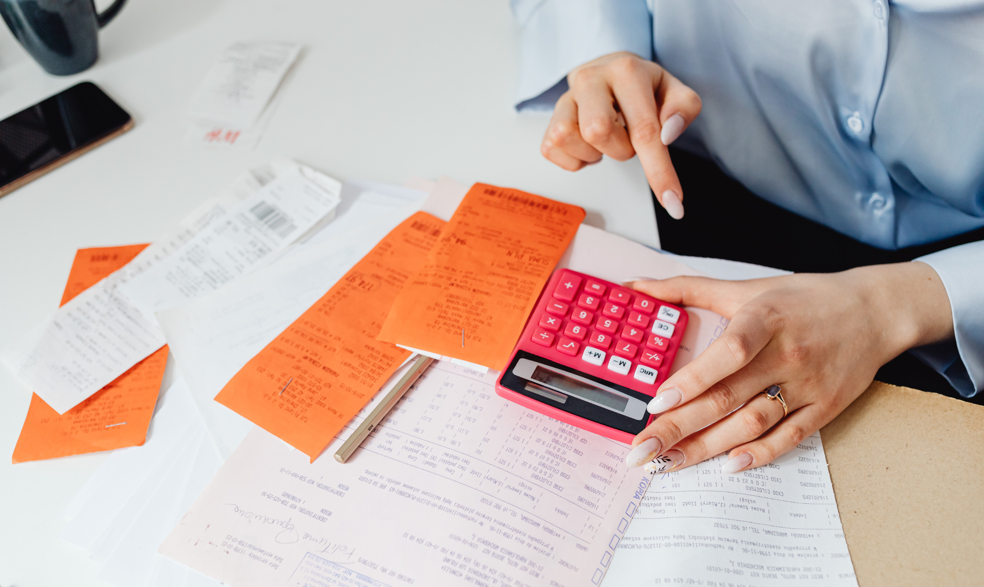 Person points at receipts with calculator, budgeting expenses on a white desk. Person points at receipts with calculator, budgeting expenses on a white desk.