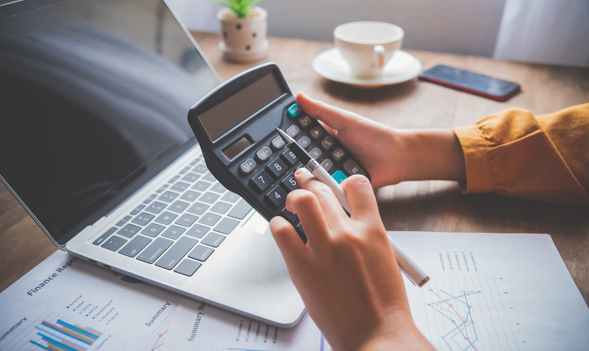 Person using a calculator with a laptop, documents, and coffee cup nearby. Person using a calculator with a laptop, documents, and coffee cup nearby.