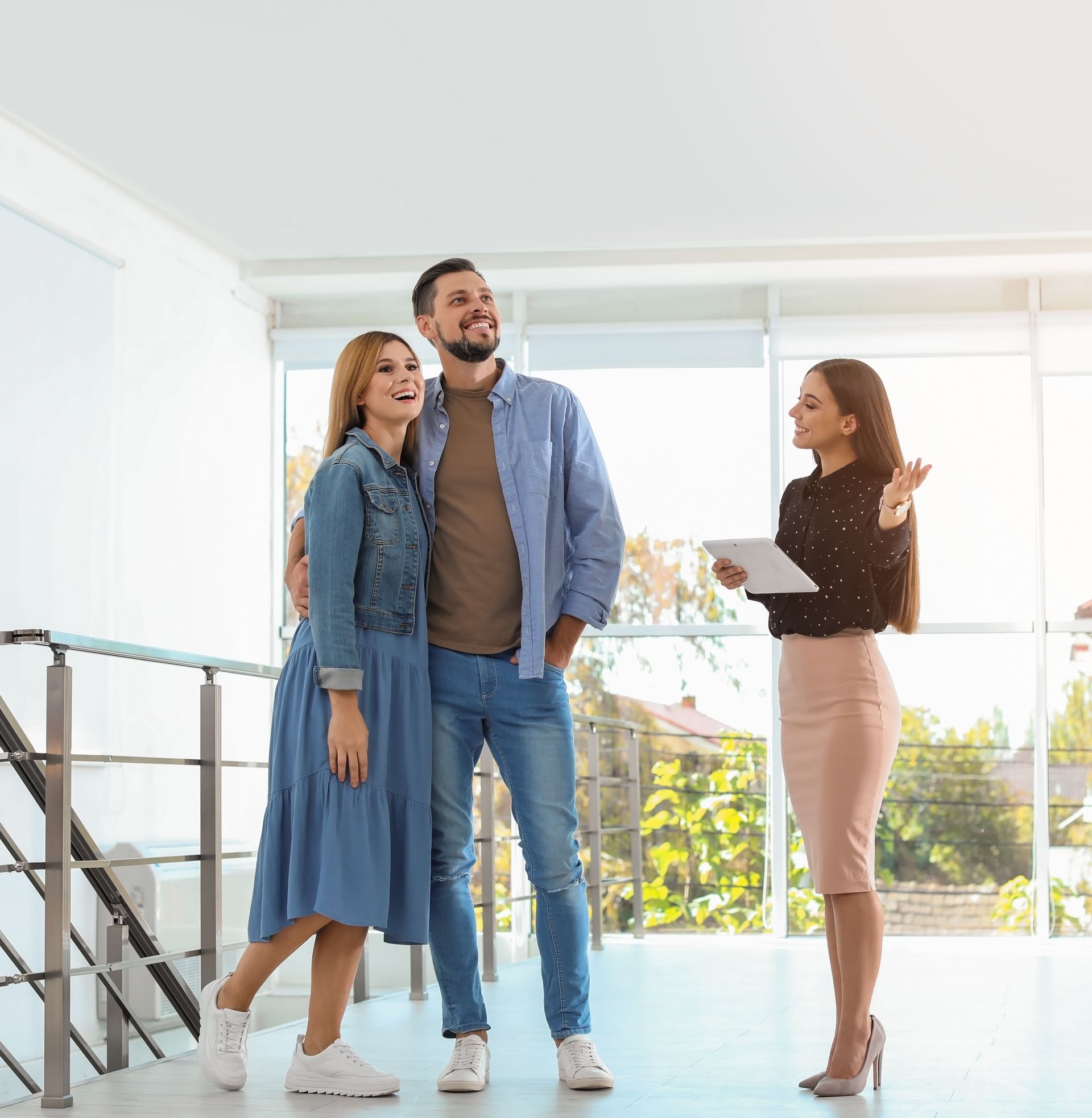 Three people standing in a bright modern home, smiling and talking near a staircase.